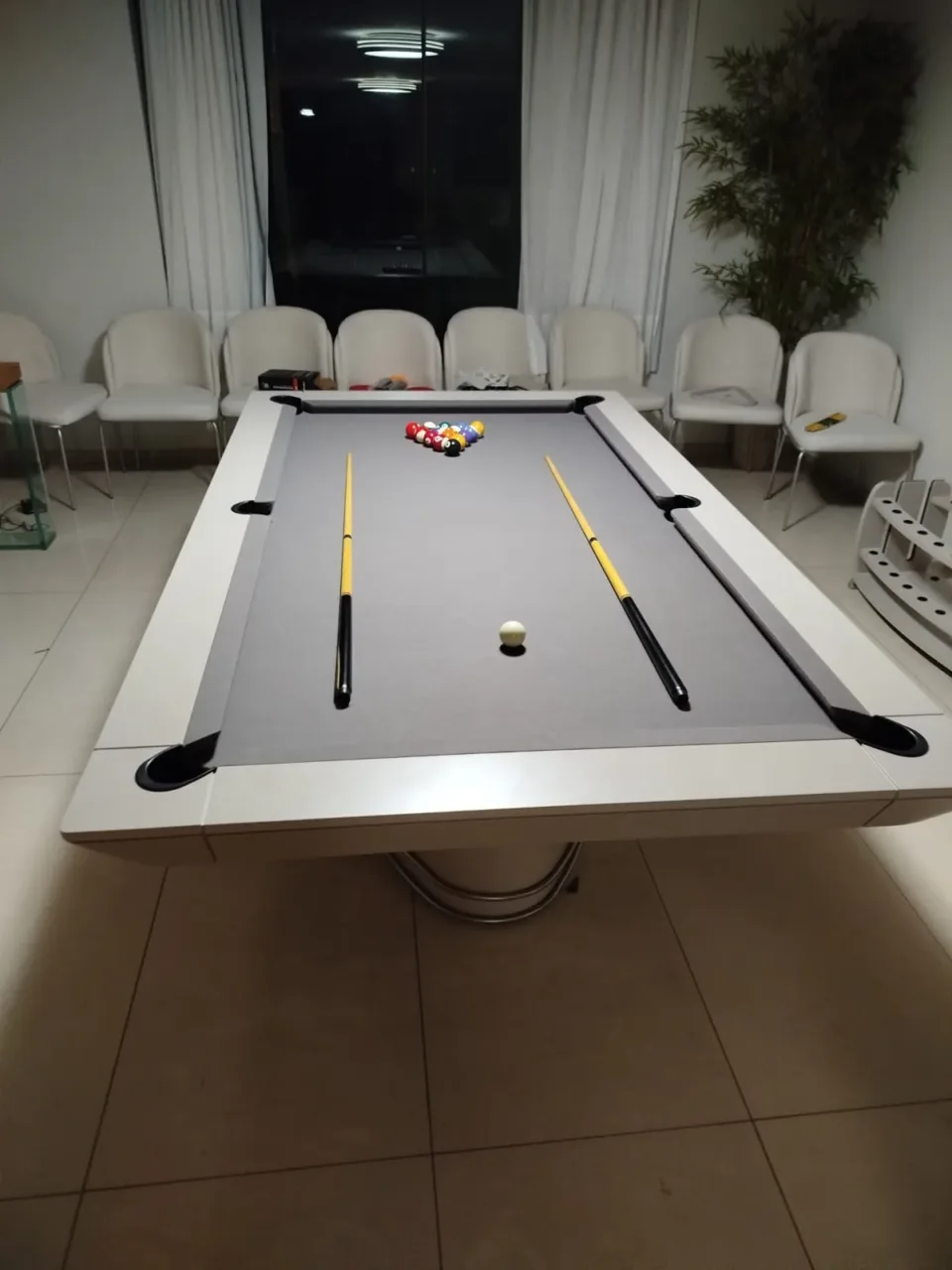 Mesa de bilhar com tecido claro e tacos sobre o tampo