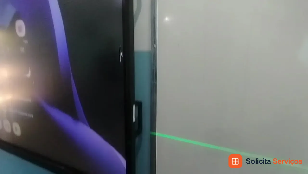Imagem do acervo mostrando a lateral da televisão e uma linha verde de referência. O enquadramento destaca o alinhamento da tela em relação à superfície ao lado. No pedido de instalação, explique a posição desejada e mostre a parede inteira. O posicionamento deve ser combinado conforme o aparelho, o suporte e o ambiente. A fotografia não identifica a cidade de execução e é apresentada como referência visual.