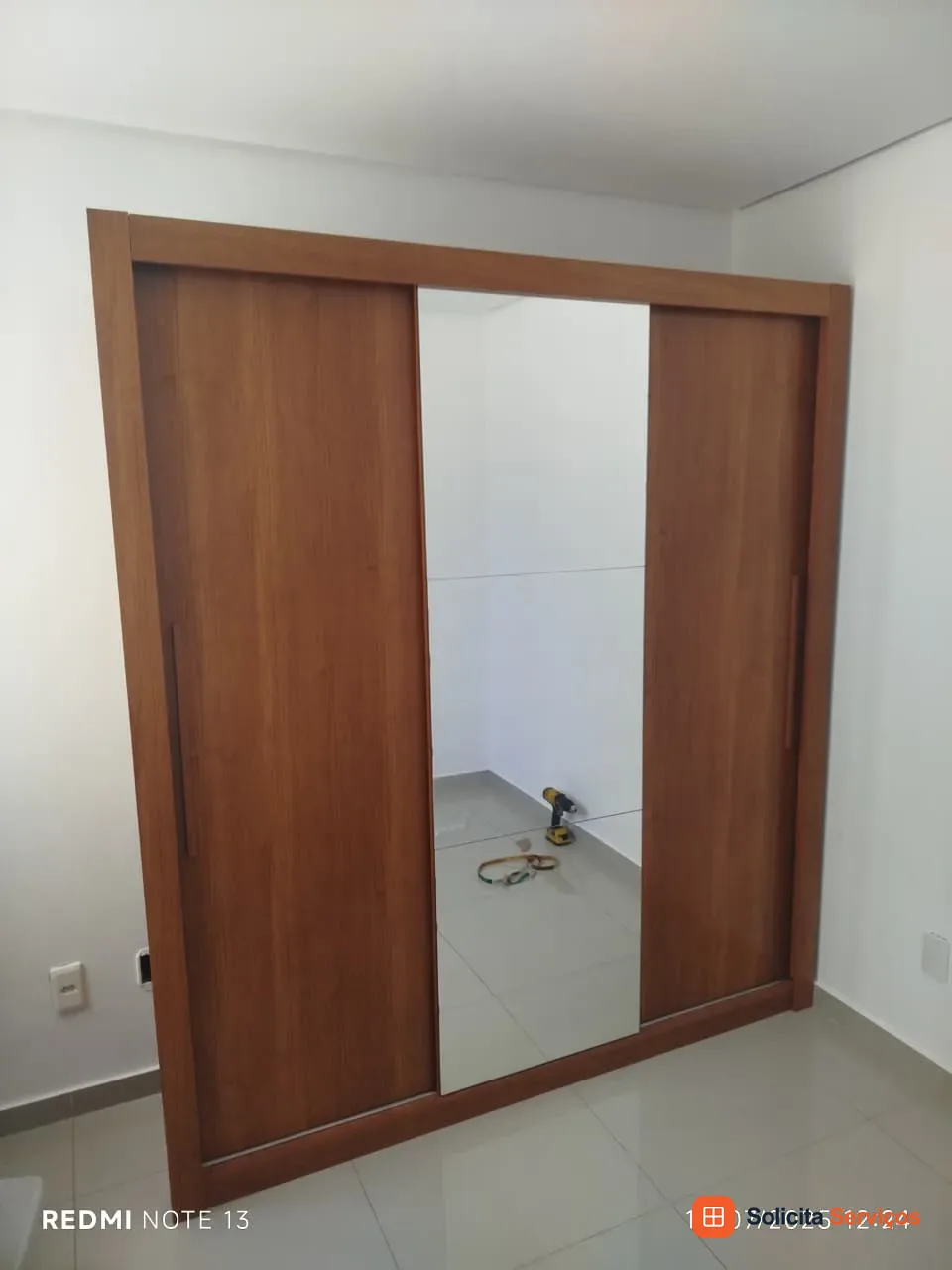 Fotografia do acervo com guarda-roupa em acabamento amadeirado. Uma das portas de correr apresenta uma faixa espelhada na frente. O enquadramento mostra a relação visual do móvel com a parede do quarto. Mostre o modelo comprado e o ambiente disponível ao consultar sua própria montagem. A fotografia não confirma compatibilidade de peças nem comprova serviço no endereço solicitado.