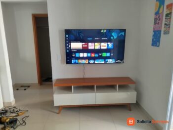 Rack claro com tampo amadeirado e televisão posicionada acima.